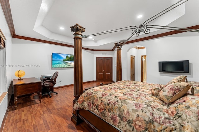 bedroom with arched walkways, a tray ceiling, recessed lighting, ornate columns, and wood finished floors