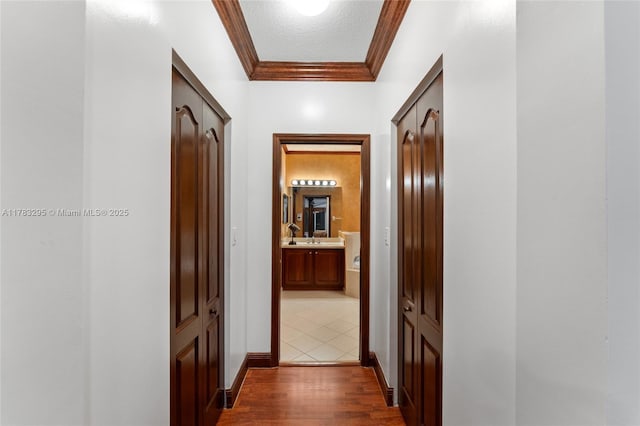 hall featuring crown molding, a sink, baseboards, and dark wood finished floors