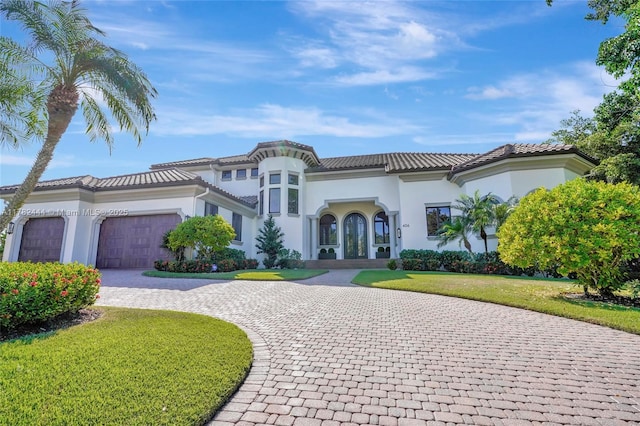 mediterranean / spanish home with stucco siding, curved driveway, an attached garage, a front lawn, and a tile roof