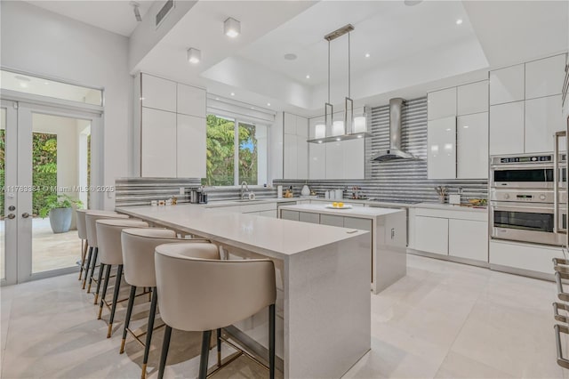 kitchen with tasteful backsplash, wall chimney range hood, white cabinetry, modern cabinets, and double oven