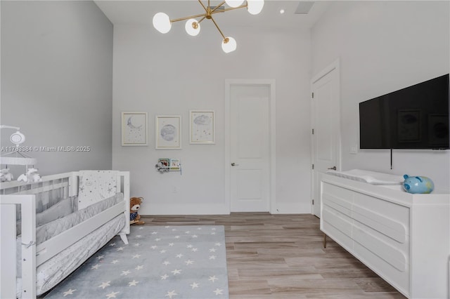 bedroom featuring visible vents, a chandelier, wood finished floors, a crib, and baseboards