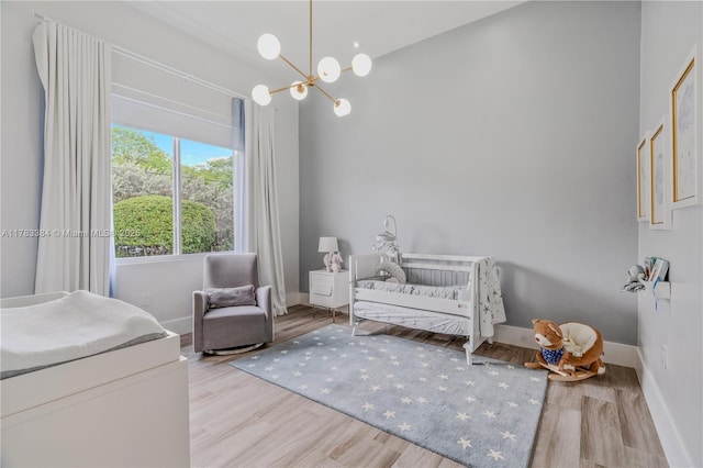 bedroom with a nursery area, baseboards, an inviting chandelier, and wood finished floors