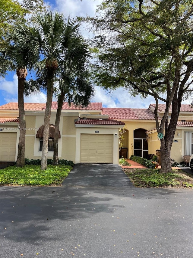 mediterranean / spanish house with aphalt driveway, stucco siding, a tiled roof, and an attached garage