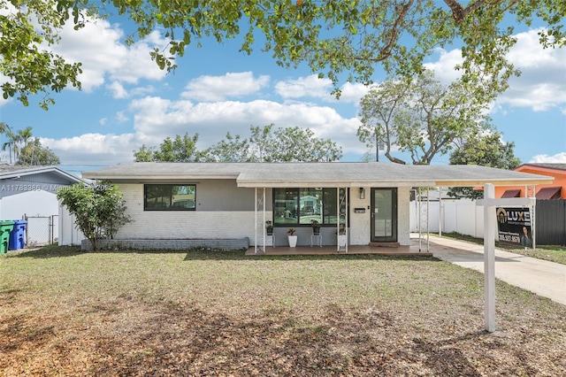 ranch-style home featuring brick siding, a front yard, fence, and a carport