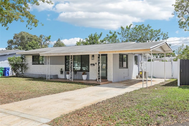 ranch-style home featuring concrete driveway, a carport, a front yard, a porch, and fence