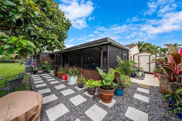 back of property with a shed, a sunroom, a yard, an outdoor structure, and a patio