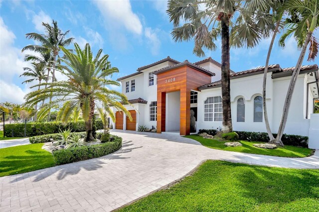 3408 NE 169th St, North Miami Beach, FL 33160 - view of front of home with stucco siding, a tiled roof, a front lawn, and curved driveway