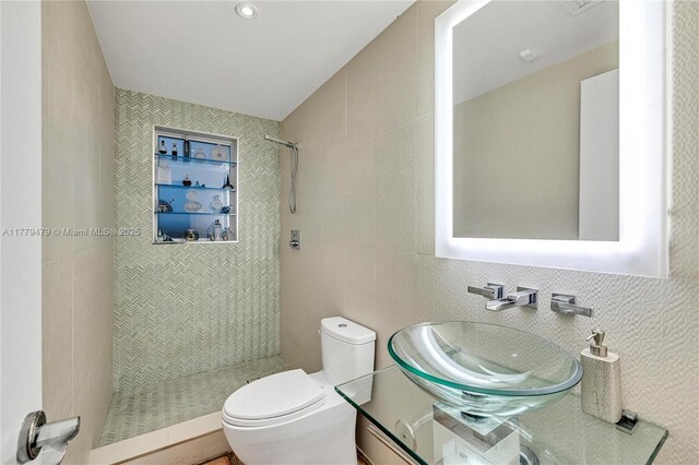 full bath featuring tile walls, a sink, a tile shower, and toilet