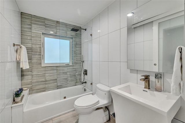 bathroom featuring a sink, tile walls, toilet, and bathtub / shower combination