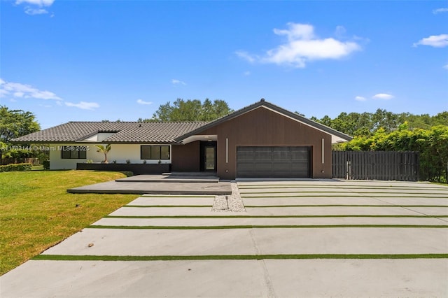 view of front facade featuring fence, an attached garage, a tile roof, concrete driveway, and a front lawn