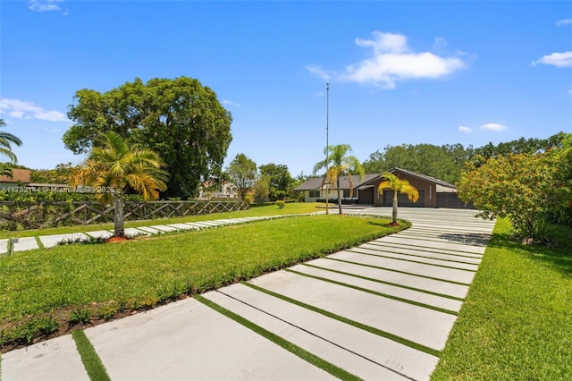 view of community featuring fence, a garage, driveway, and a lawn