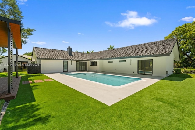 exterior space featuring a lawn, a chimney, an outdoor pool, stucco siding, and a tile roof