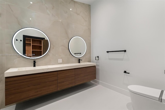 bathroom featuring double vanity, toilet, tile walls, and baseboards