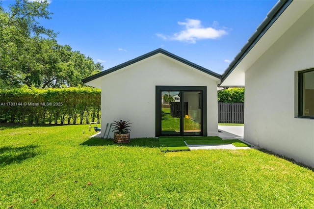 back of property featuring stucco siding, an outdoor structure, fence, and a lawn