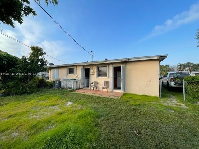 rear view of property with central AC, stucco siding, and a lawn