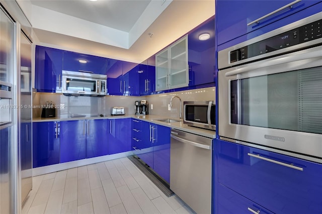 kitchen with modern cabinets, glass insert cabinets, light countertops, a sink, and stainless steel appliances
