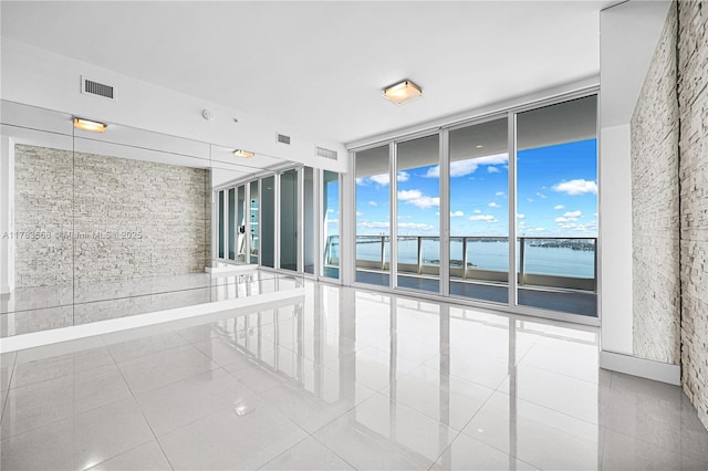 spare room with tile patterned floors, floor to ceiling windows, visible vents, and a water view