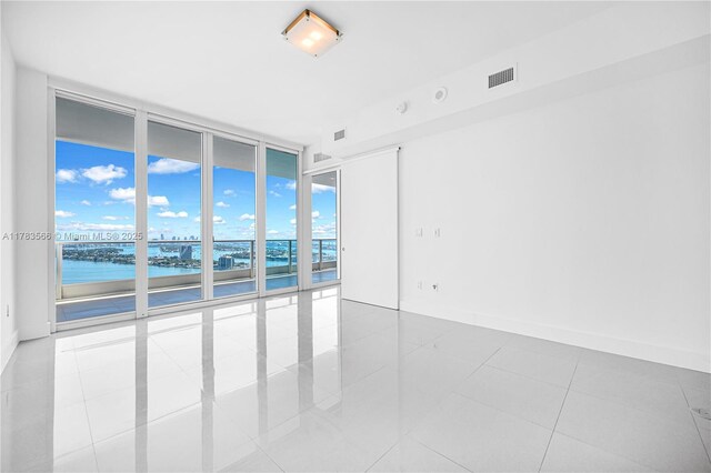 tiled spare room featuring floor to ceiling windows, visible vents, a water view, and baseboards