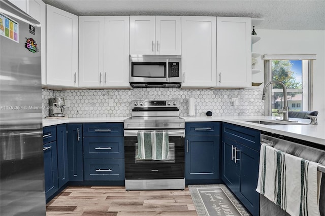 kitchen with open shelves, a sink, light countertops, appliances with stainless steel finishes, and blue cabinets