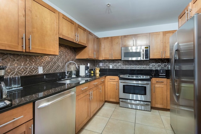 kitchen with appliances with stainless steel finishes, light tile patterned floors, brown cabinets, decorative backsplash, and a sink