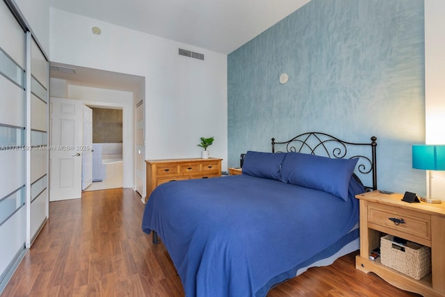 bedroom with wallpapered walls, connected bathroom, visible vents, an accent wall, and wood finished floors