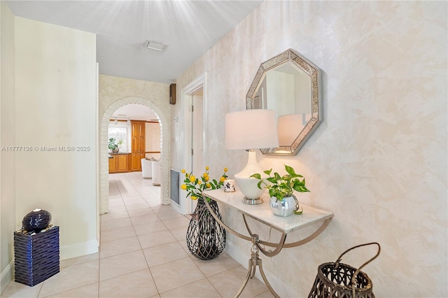 hall featuring baseboards, wallpapered walls, arched walkways, and visible vents