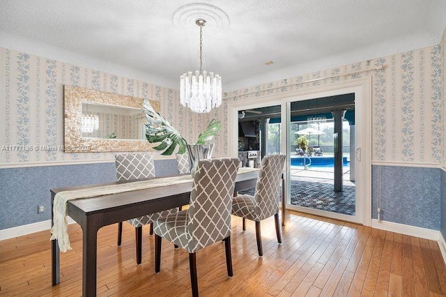 dining room featuring an inviting chandelier, hardwood / wood-style floors, wallpapered walls, and baseboards
