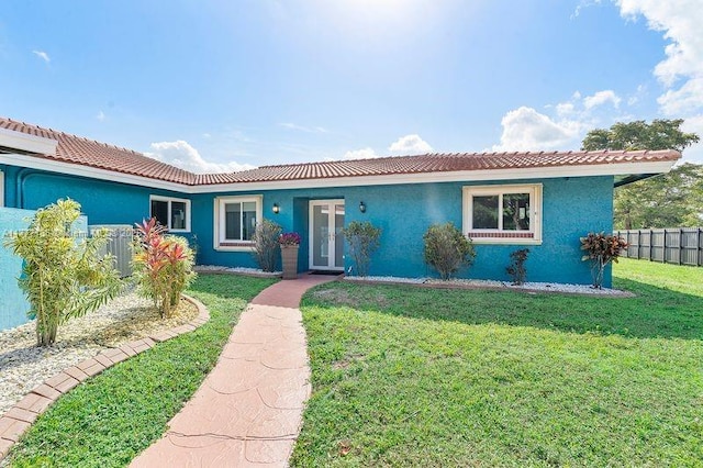 ranch-style house with a front lawn, stucco siding, french doors, and fence