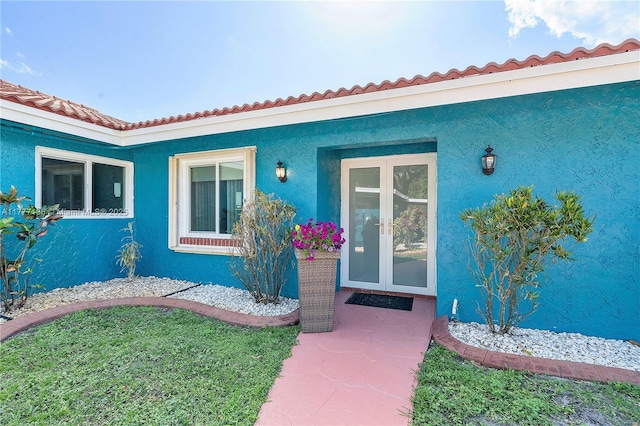 doorway to property with stucco siding, a tiled roof, and french doors