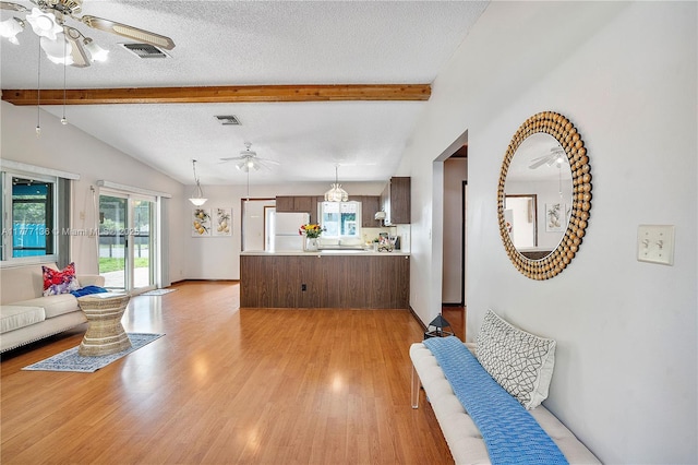 living area with a textured ceiling, light wood-style flooring, visible vents, a ceiling fan, and vaulted ceiling with beams