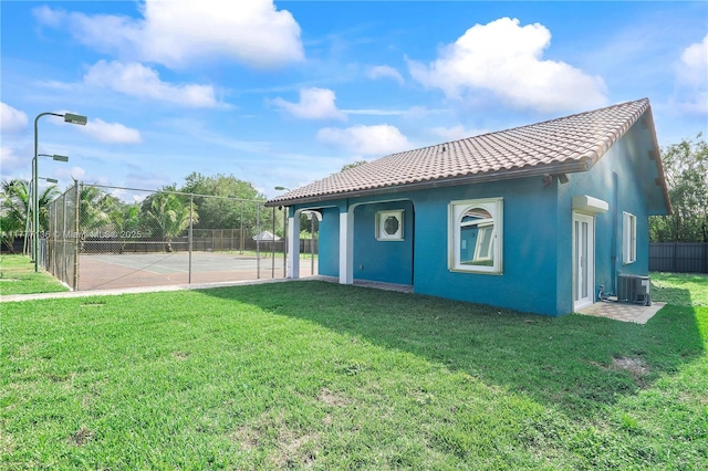 rear view of property with a yard, stucco siding, a tiled roof, and fence