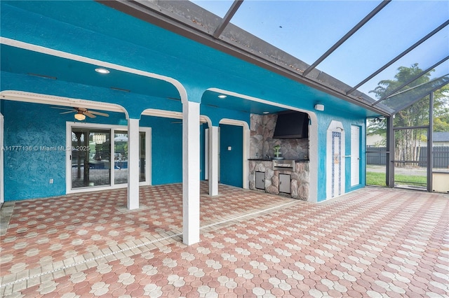 view of patio / terrace with fence, a ceiling fan, glass enclosure, and an outdoor kitchen