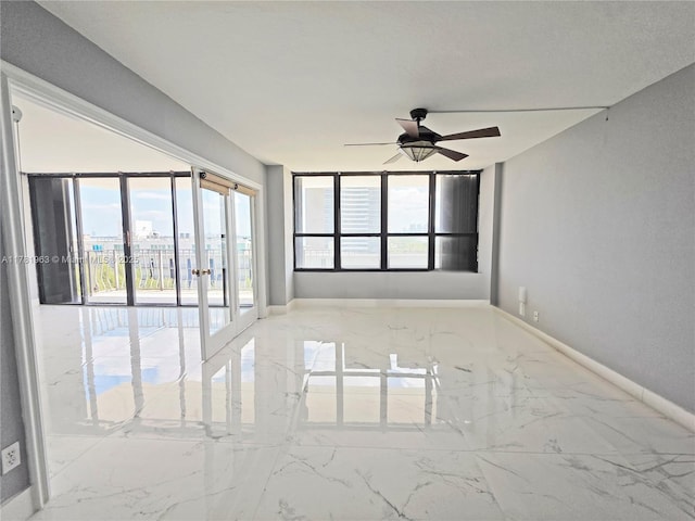 unfurnished room featuring baseboards, marble finish floor, ceiling fan, and a wealth of natural light