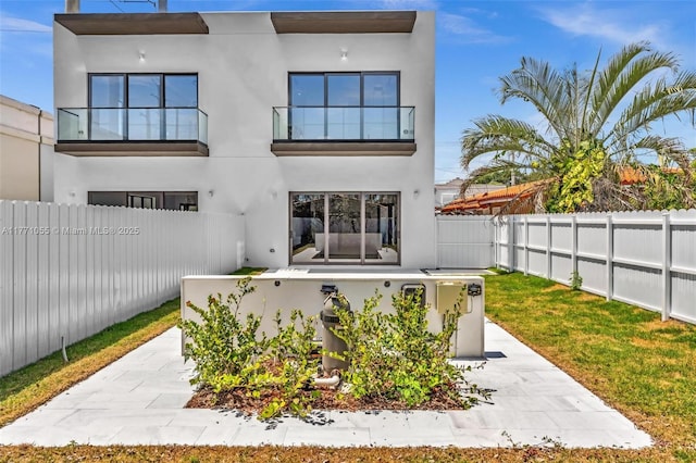 back of property featuring a fenced backyard, a balcony, and stucco siding