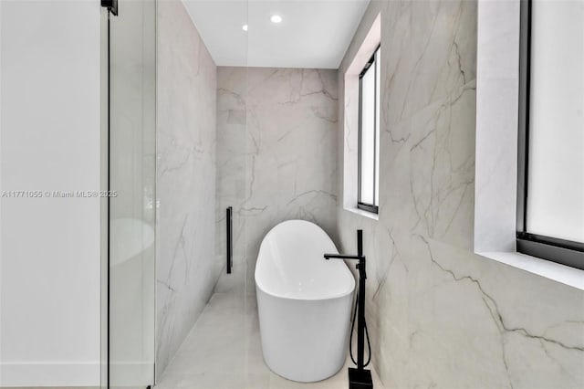 bathroom featuring recessed lighting, a freestanding tub, tile walls, and a healthy amount of sunlight
