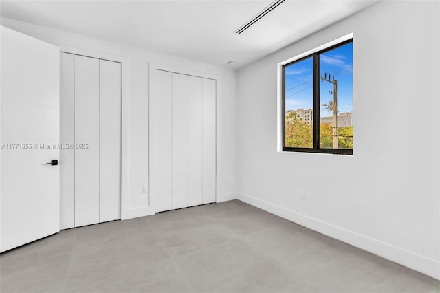 unfurnished bedroom with finished concrete flooring, two closets, baseboards, and visible vents