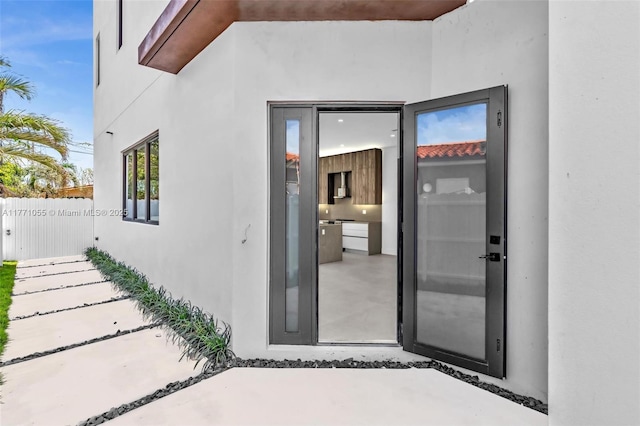 view of exterior entry with fence and stucco siding