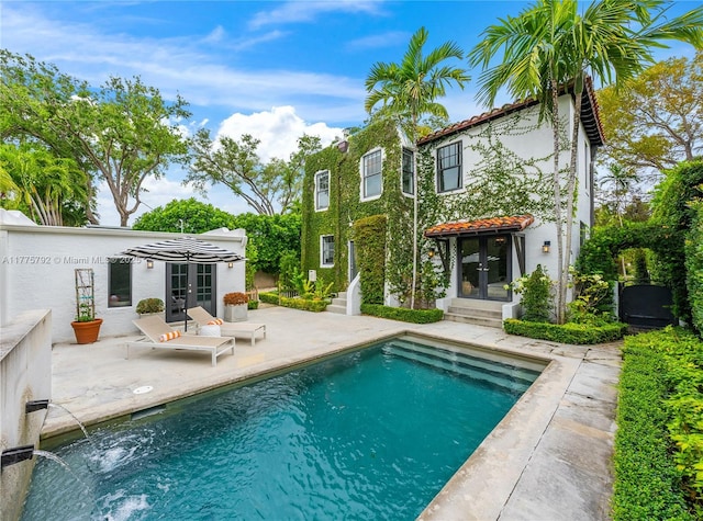 rear view of property featuring a patio, stucco siding, an outdoor pool, french doors, and a tiled roof