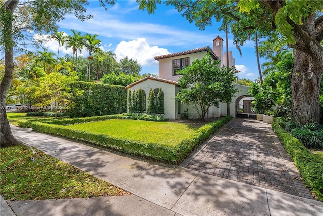 view of front facade featuring a front yard, a chimney, a tile roof, stucco siding, and a gate