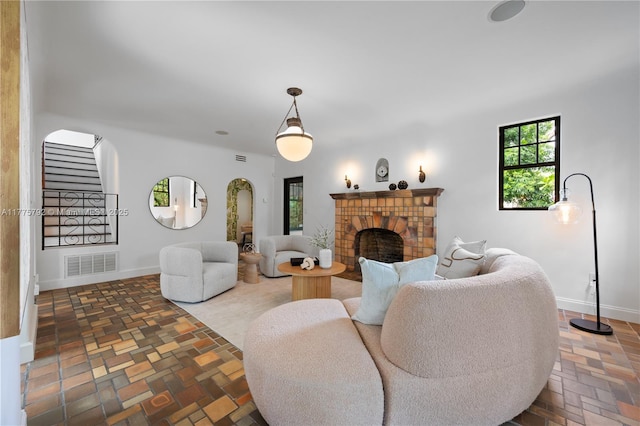 living area featuring visible vents, baseboards, a brick fireplace, and stairs