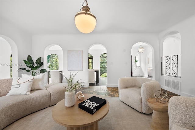 living room with arched walkways, visible vents, stone tile floors, and baseboards