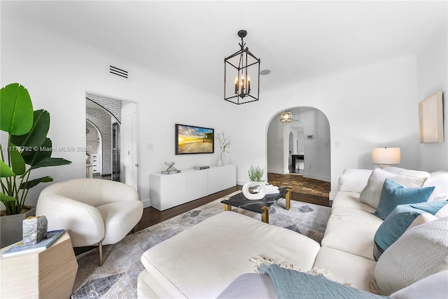 living area with visible vents, baseboards, arched walkways, a chandelier, and wood finished floors