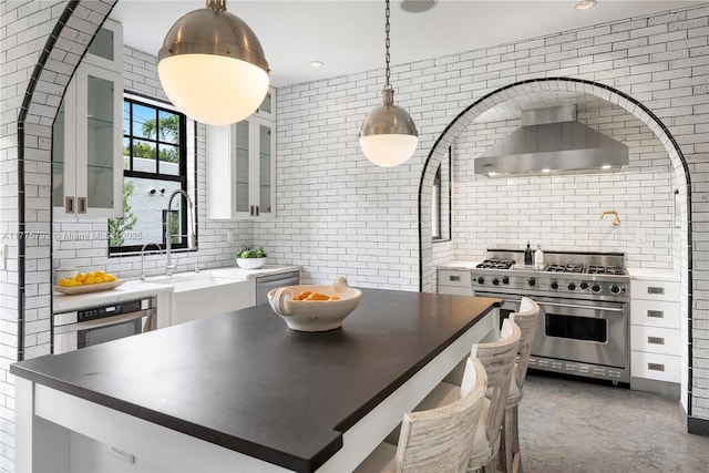 kitchen with tasteful backsplash, white cabinetry, wall chimney exhaust hood, appliances with stainless steel finishes, and hanging light fixtures
