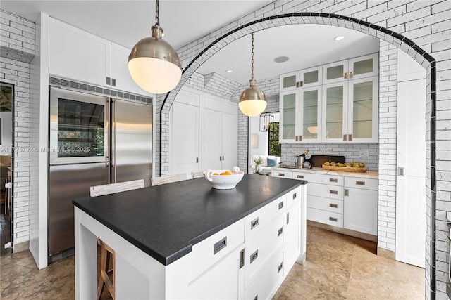 kitchen featuring glass insert cabinets, dark countertops, white cabinets, arched walkways, and stainless steel built in fridge