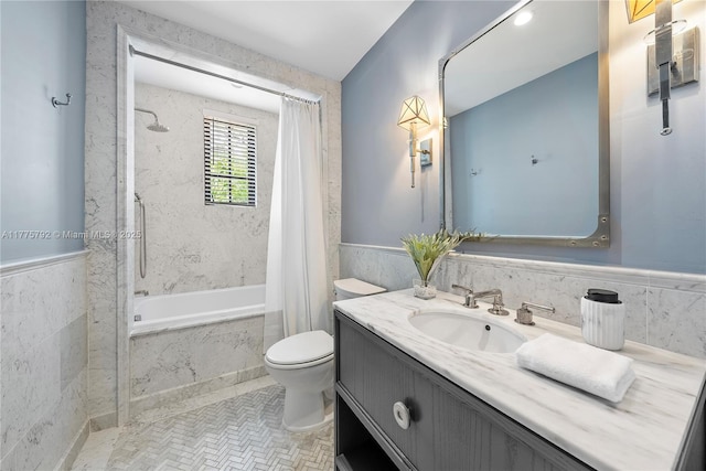 bathroom featuring a combined bath / shower with marble appearance, vanity, toilet, wainscoting, and tile walls