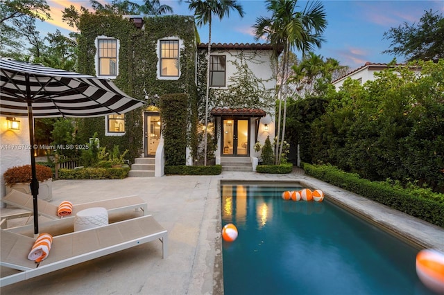 back of house at dusk featuring a patio, an outdoor pool, and a tiled roof