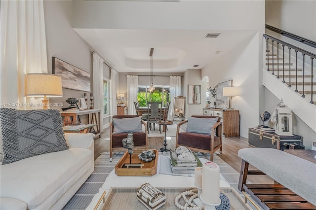 living area with stairway, wood finished floors, a raised ceiling, baseboards, and visible vents