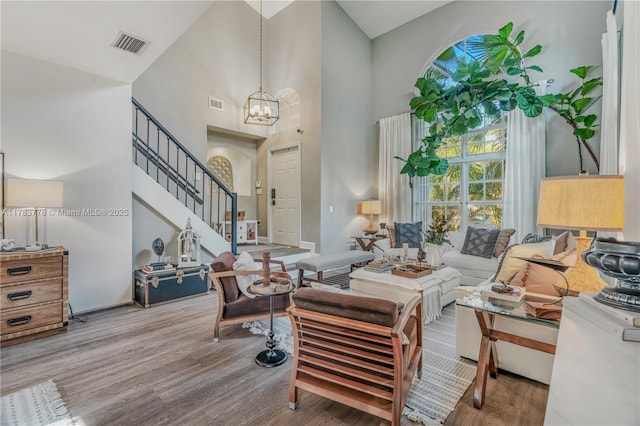 living room featuring a chandelier, wood finished floors, visible vents, and a high ceiling