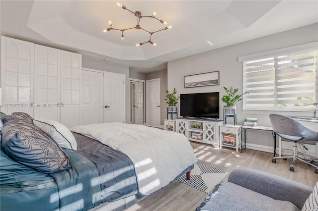 bedroom with a raised ceiling, wood finished floors, baseboards, and a notable chandelier
