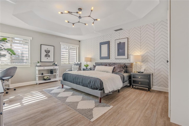 bedroom with an accent wall, wallpapered walls, a tray ceiling, light wood-style flooring, and baseboards